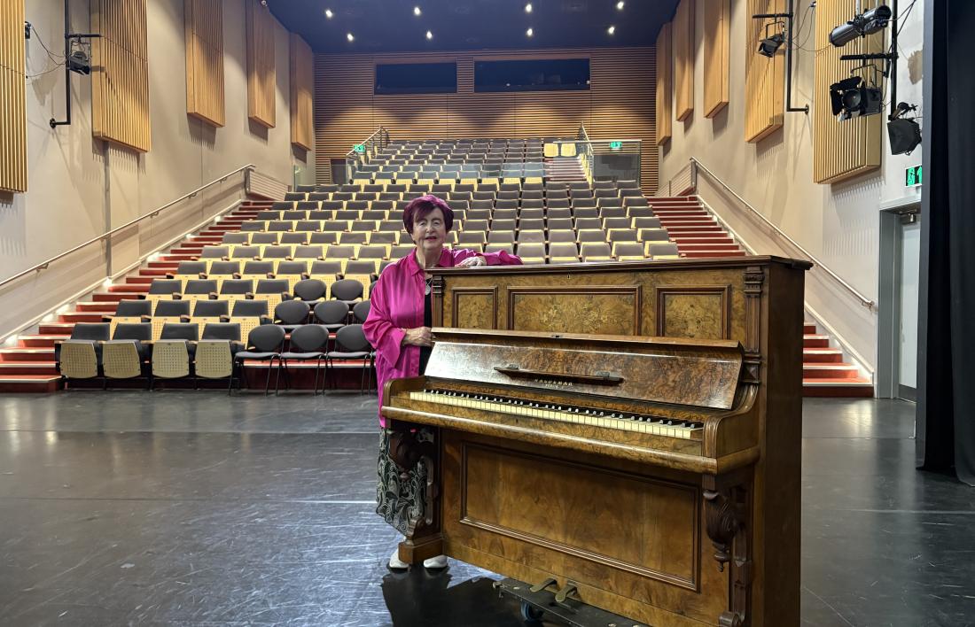 Woman in pink shirt standing beside an upright piano in Auditorium